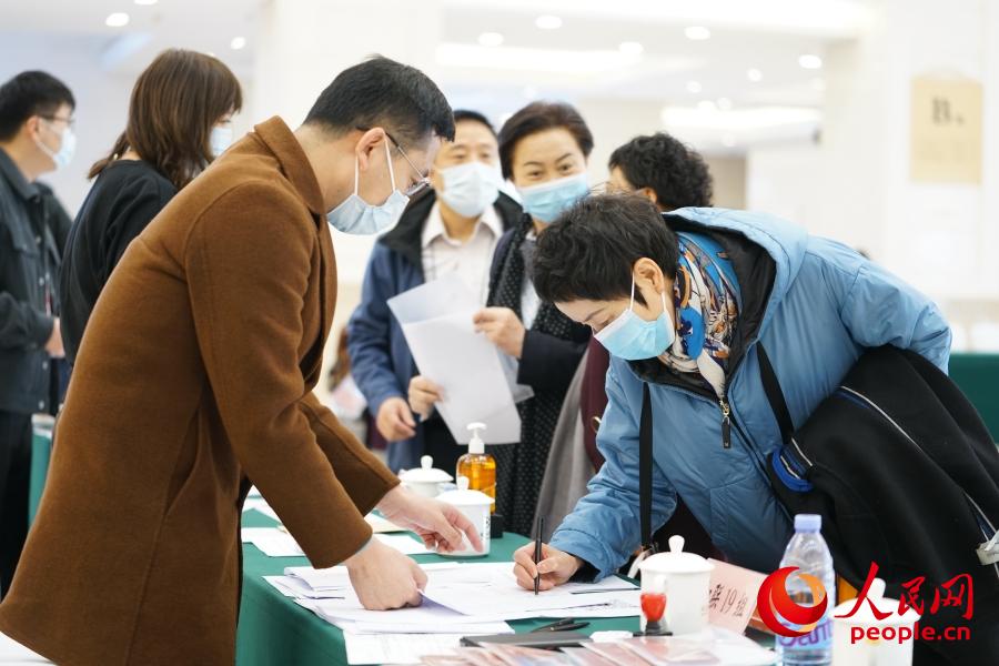 3月2日，在北京会议中心驻地，前来报到的全国政协委员在工作人员的引导下签到、领取证件和会议资料。人民网记者 王天乐摄